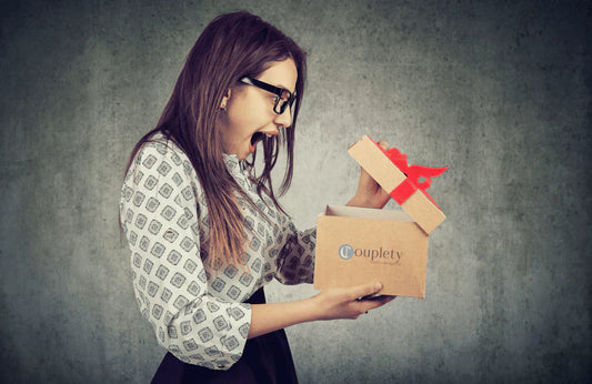 Überraschte Frau mit Brille öffnet eine Geschenkschachtel mit roter Schleife und freut sich über den Inhalt – sinnvolle Geschenkidee für Frauen.